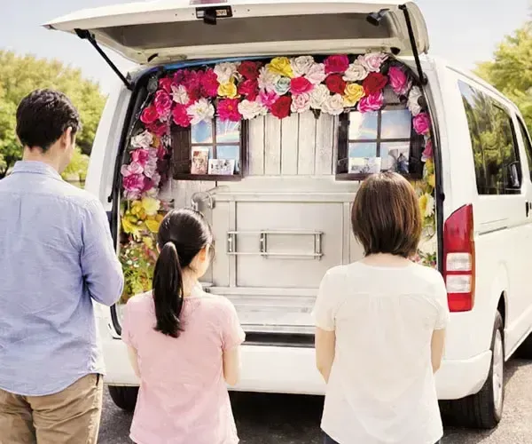 花で飾られた移動火葬車で見送る家族